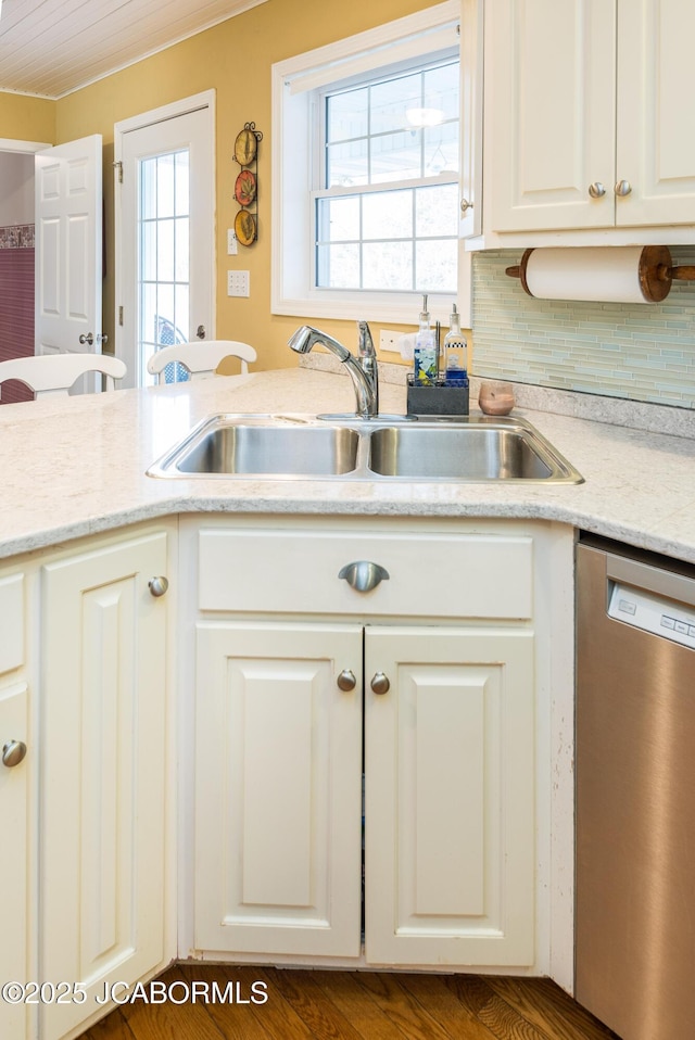 kitchen featuring tasteful backsplash, stainless steel dishwasher, a sink, and white cabinets