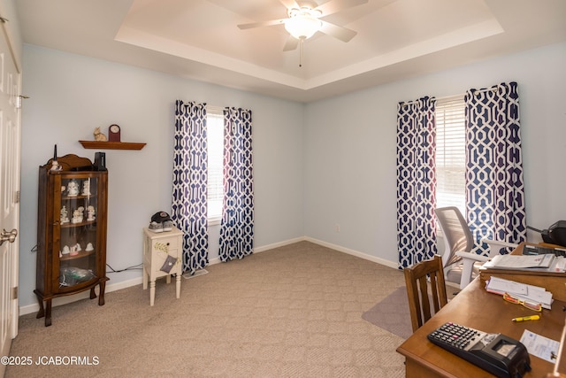 home office with a tray ceiling, light colored carpet, ceiling fan, and baseboards