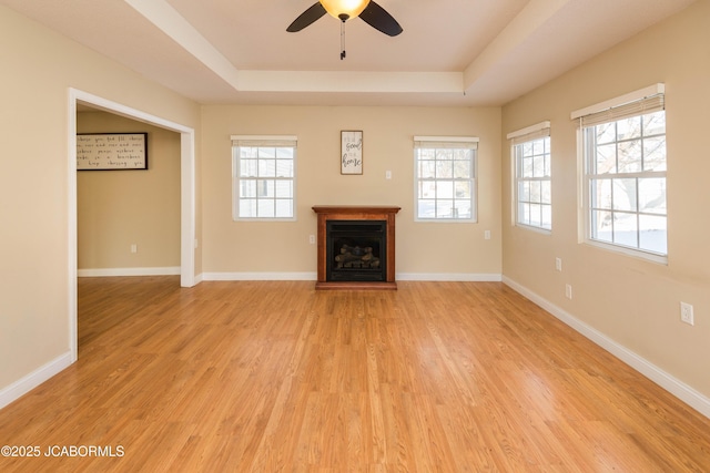 unfurnished living room featuring a fireplace, a tray ceiling, and a wealth of natural light