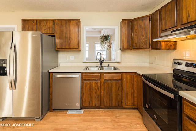 kitchen with light wood-style floors, appliances with stainless steel finishes, light countertops, under cabinet range hood, and a sink