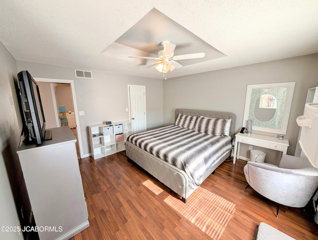 bedroom with ceiling fan, a tray ceiling, dark hardwood / wood-style floors, and a textured ceiling