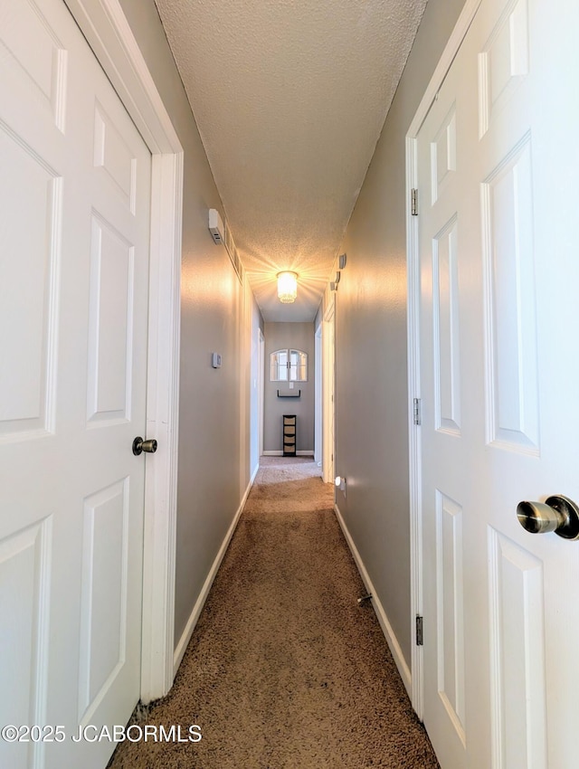 hallway with dark carpet and a textured ceiling