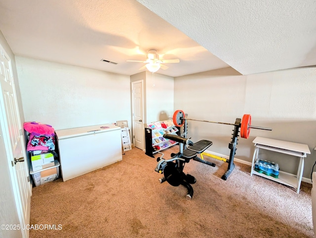 exercise area featuring light carpet, ceiling fan, and a textured ceiling