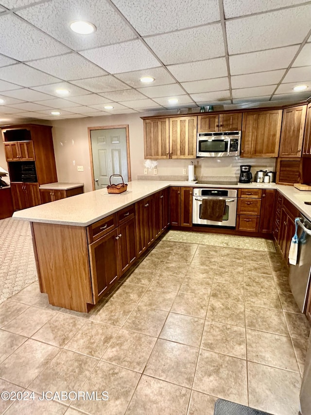 kitchen featuring kitchen peninsula, a drop ceiling, light tile patterned floors, and stainless steel appliances