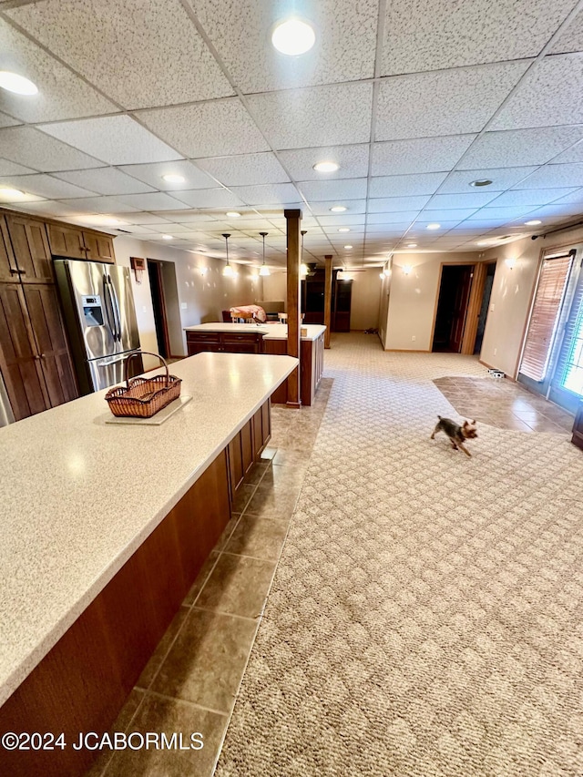 interior space with a drop ceiling, stainless steel fridge with ice dispenser, and hanging light fixtures