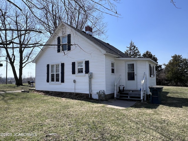 back of property featuring entry steps, a chimney, and a lawn