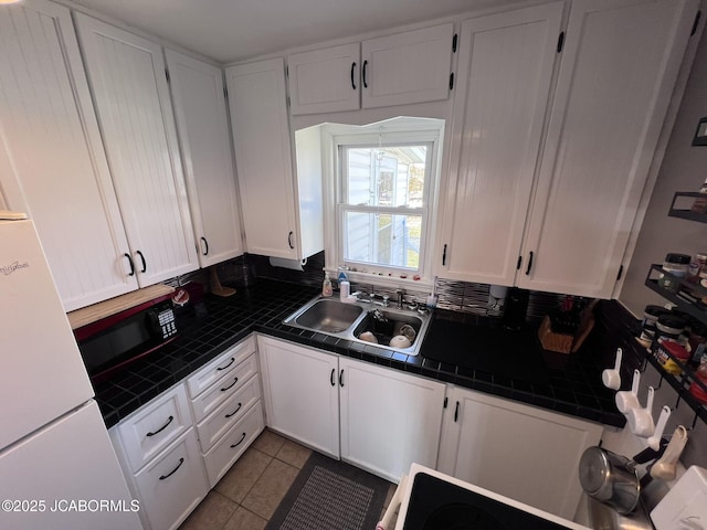 kitchen with a sink, tile counters, white cabinets, and freestanding refrigerator