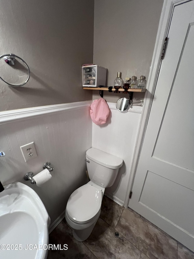 bathroom with toilet, tile patterned floors, and wainscoting