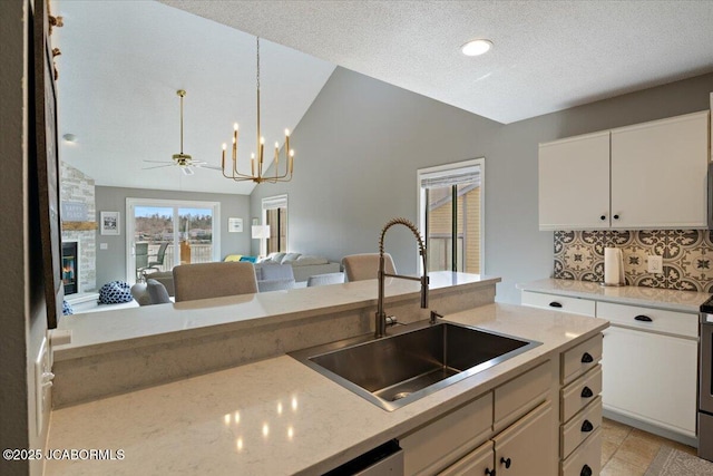 kitchen with lofted ceiling, a sink, a stone fireplace, open floor plan, and backsplash