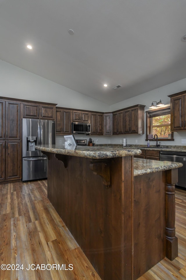 kitchen with lofted ceiling, dark hardwood / wood-style floors, light stone countertops, appliances with stainless steel finishes, and a kitchen island