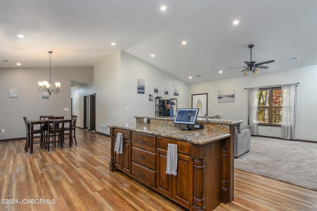 kitchen with pendant lighting, vaulted ceiling, light wood-type flooring, light stone countertops, and a kitchen island