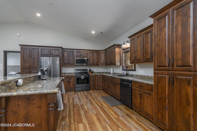 kitchen featuring sink, vaulted ceiling, light stone countertops, light hardwood / wood-style floors, and stainless steel appliances