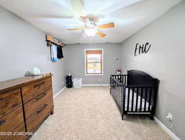 bedroom featuring baseboards, ceiling fan, a nursery area, and light colored carpet