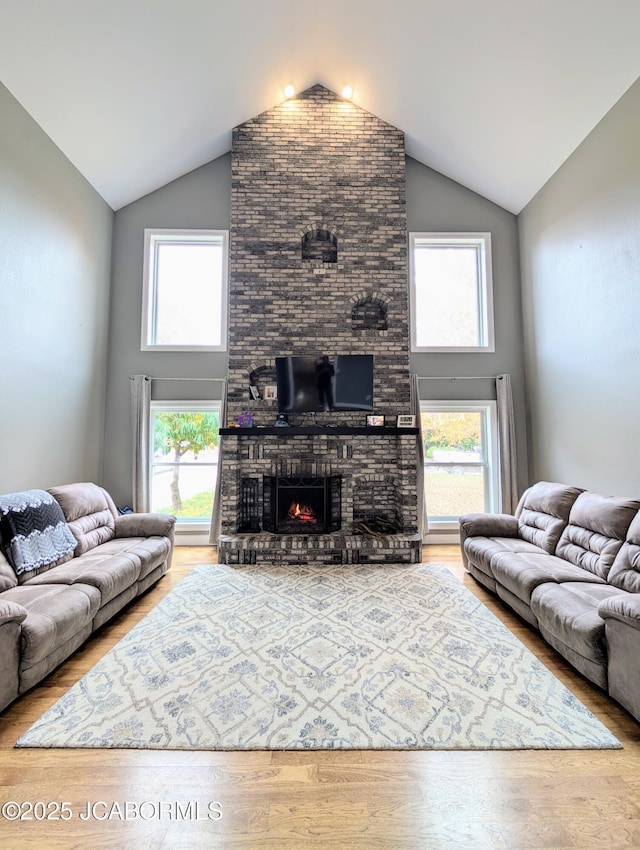 living area with a brick fireplace, high vaulted ceiling, and wood finished floors