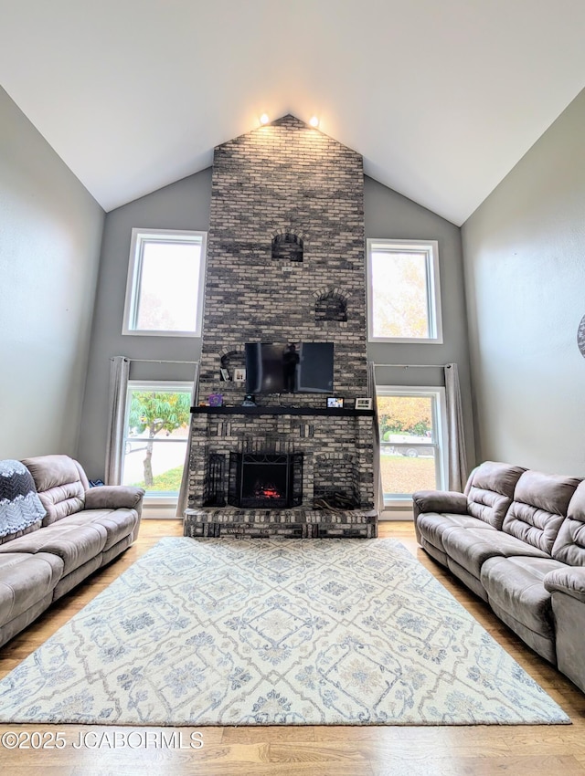 living area featuring a brick fireplace, high vaulted ceiling, and wood finished floors