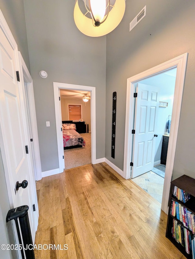 hall featuring light wood-type flooring, visible vents, a towering ceiling, and baseboards