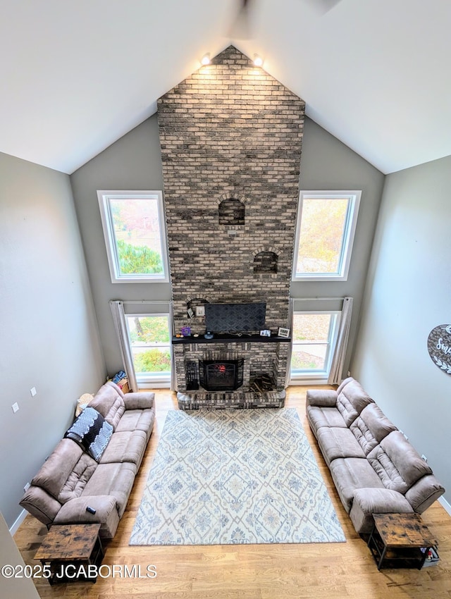 living area with high vaulted ceiling, a brick fireplace, and wood finished floors