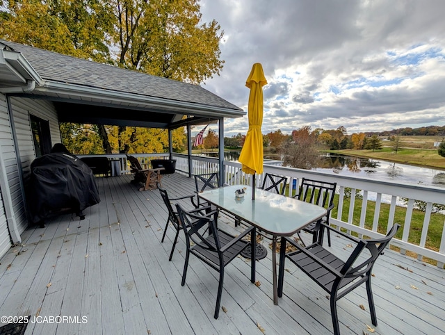 wooden terrace with outdoor dining space, grilling area, and a water view