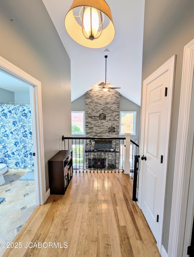 hall with high vaulted ceiling, a healthy amount of sunlight, baseboards, and wood finished floors