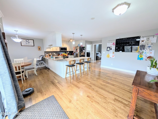 kitchen with light wood finished floors, decorative backsplash, appliances with stainless steel finishes, a peninsula, and a sink