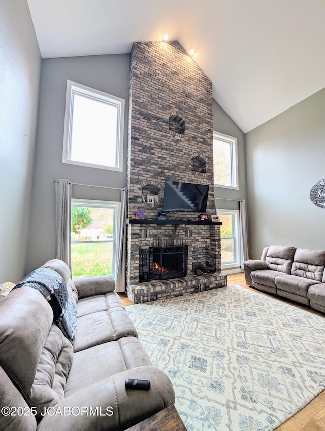 living area with high vaulted ceiling, a fireplace, and wood finished floors