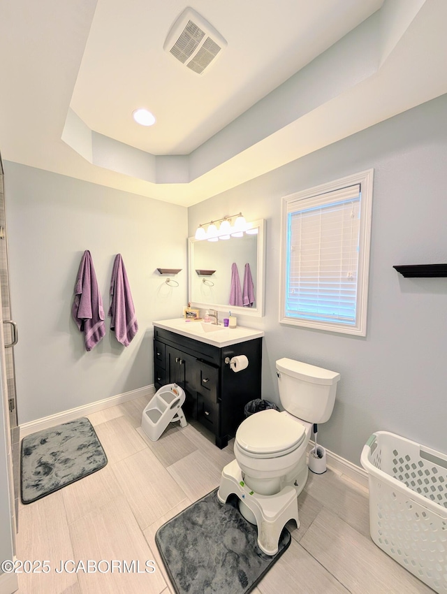 bathroom with toilet, vanity, visible vents, baseboards, and a tray ceiling