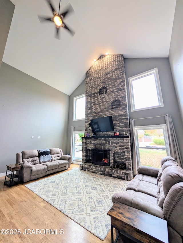 living area featuring high vaulted ceiling, a brick fireplace, ceiling fan, and wood finished floors