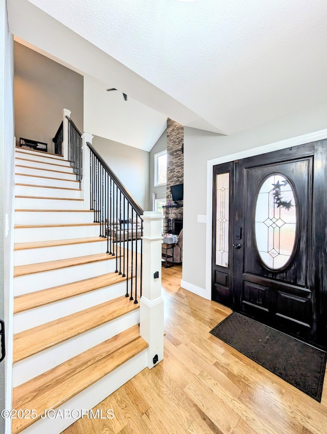 foyer featuring lofted ceiling, a textured ceiling, wood finished floors, baseboards, and stairway