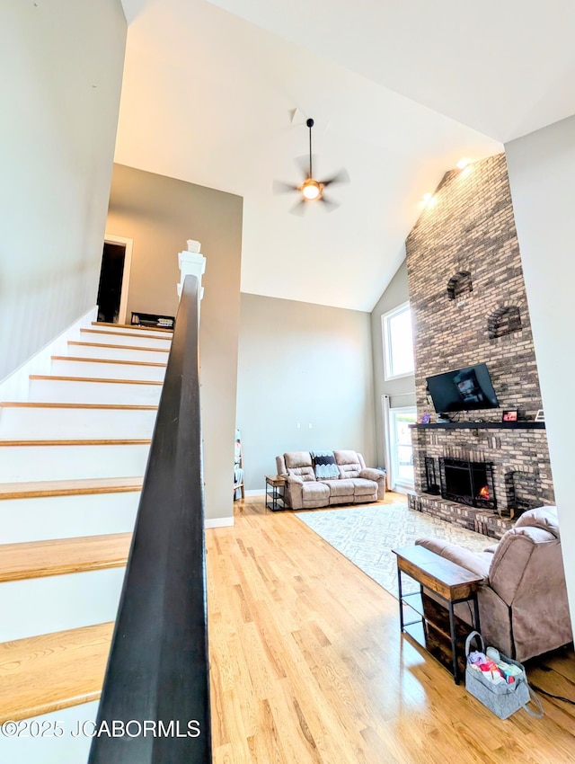 living area with ceiling fan, high vaulted ceiling, a fireplace, wood finished floors, and stairway