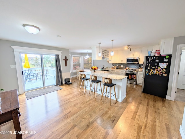 kitchen with a peninsula, a breakfast bar, a sink, appliances with stainless steel finishes, and light wood-type flooring