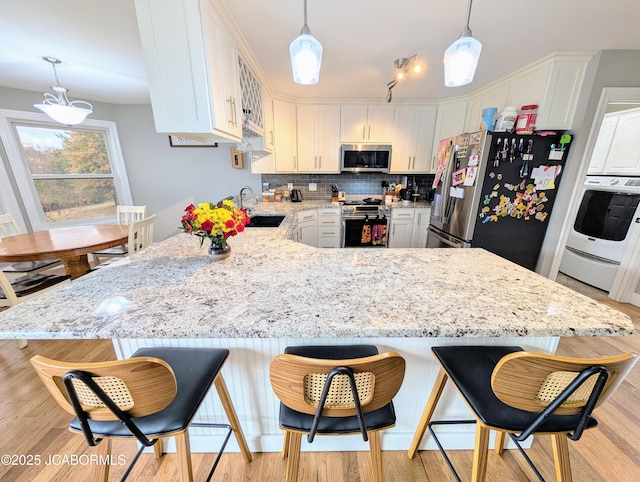 kitchen with stacked washer / drying machine, appliances with stainless steel finishes, white cabinets, a sink, and a peninsula