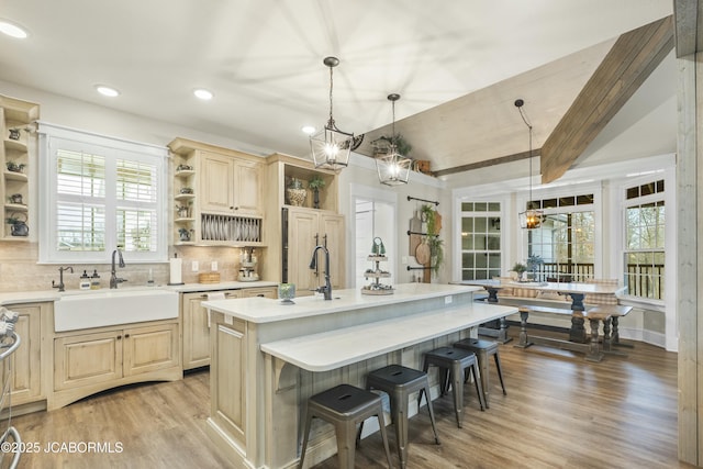 kitchen featuring a kitchen bar, sink, decorative light fixtures, a center island with sink, and vaulted ceiling with beams