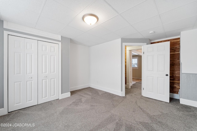 unfurnished bedroom featuring carpet flooring, a drop ceiling, a closet, and wood walls