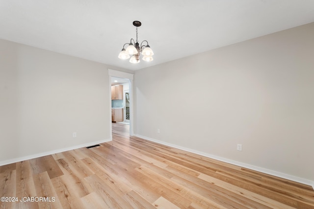 unfurnished room with light wood-type flooring and an inviting chandelier