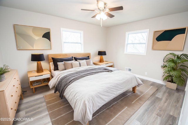 bedroom with multiple windows, ceiling fan, visible vents, and wood finished floors