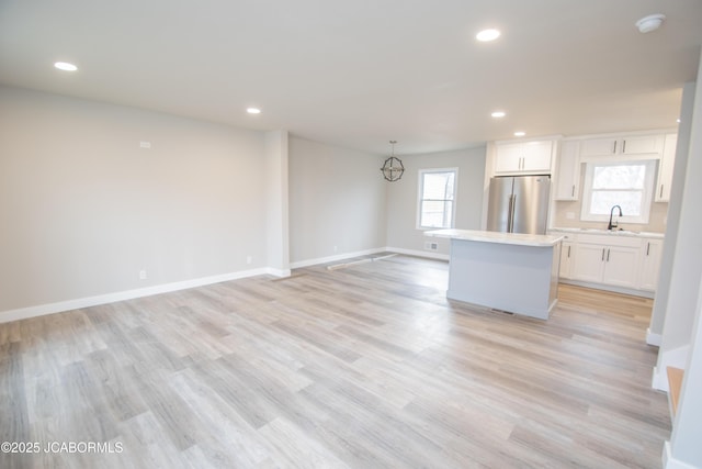 kitchen with white cabinets, a center island, hanging light fixtures, freestanding refrigerator, and light countertops