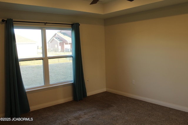 unfurnished room with a ceiling fan, dark colored carpet, and baseboards