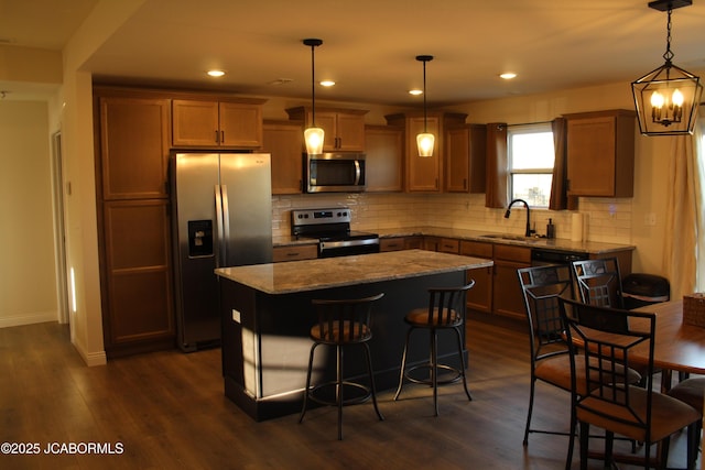 kitchen featuring light stone counters, a sink, dark wood-type flooring, appliances with stainless steel finishes, and a center island