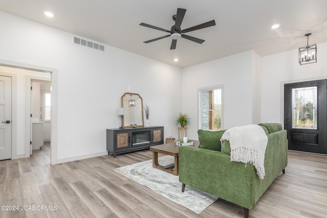 living room featuring ceiling fan with notable chandelier, a healthy amount of sunlight, and light wood-type flooring