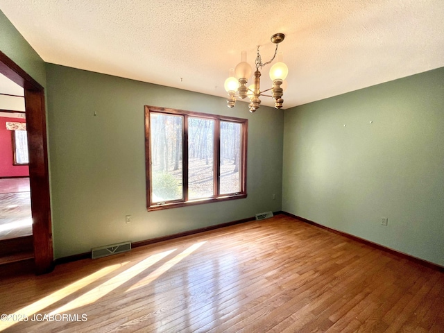 spare room featuring baseboards, visible vents, an inviting chandelier, and hardwood / wood-style flooring