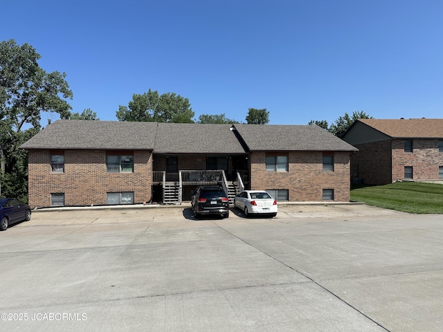 single story home featuring uncovered parking, brick siding, a shingled roof, and stairs