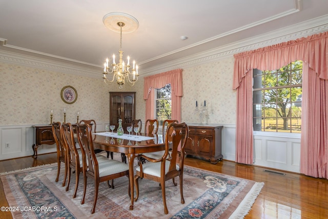 dining area with wood-type flooring, an inviting chandelier, and crown molding