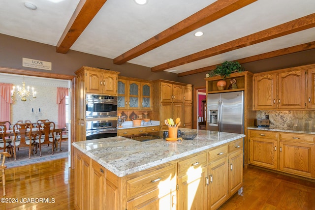 kitchen with beam ceiling, an inviting chandelier, wood-type flooring, a kitchen island, and appliances with stainless steel finishes