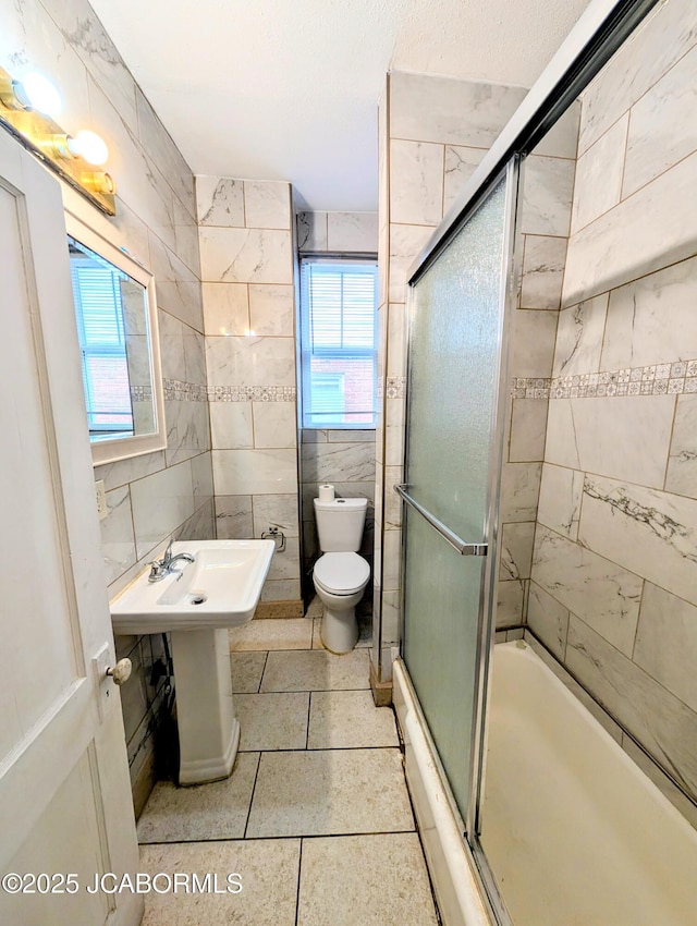 bathroom featuring tile patterned floors, toilet, a shower with door, and tile walls