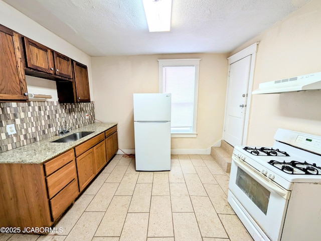 kitchen with sink, decorative backsplash, white appliances, light stone counters, and a textured ceiling