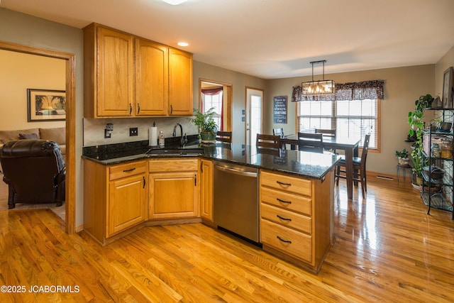 kitchen featuring a sink, a peninsula, stainless steel dishwasher, and light wood finished floors