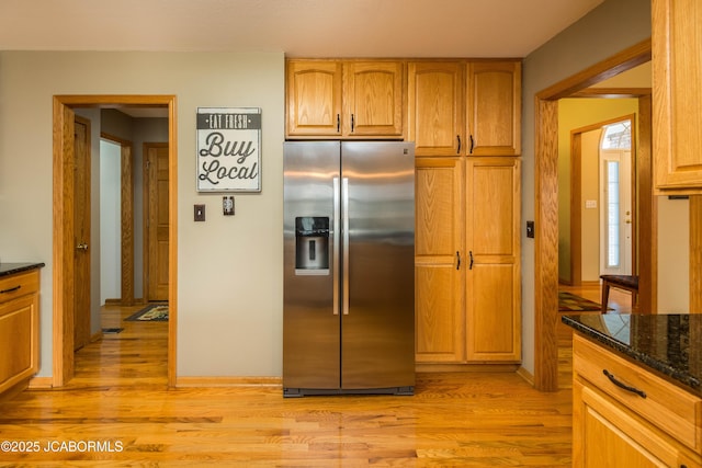 kitchen with light wood-style flooring, baseboards, stainless steel fridge with ice dispenser, brown cabinetry, and dark stone countertops