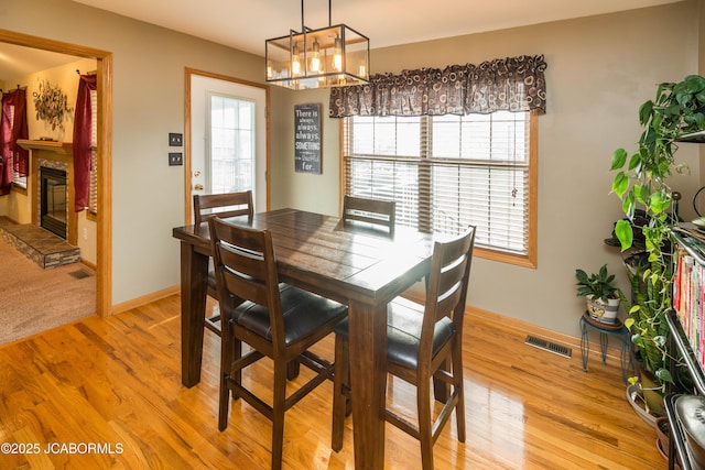 dining room with light wood-type flooring, a glass covered fireplace, visible vents, and baseboards