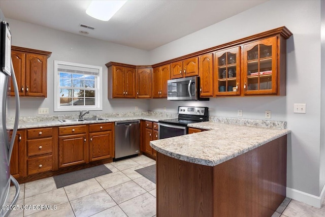 kitchen with a peninsula, a sink, light countertops, appliances with stainless steel finishes, and brown cabinets