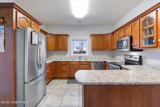 kitchen featuring appliances with stainless steel finishes, brown cabinets, glass insert cabinets, and a peninsula